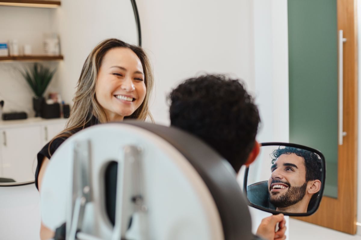 A patient checking his hair in a mirror with a team member at the clinic