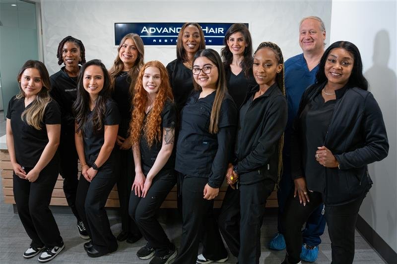 Eleven members of the Advanced Hair Restoration® Atlanta team, ten dressed in black and one in blue scrubs, standing together in front of the clinic's wall sign